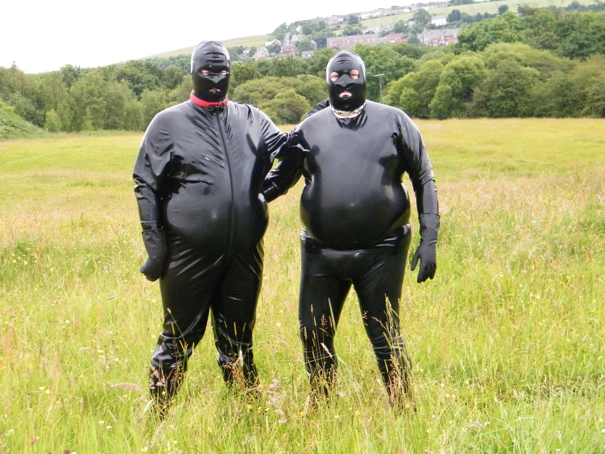 Two individuals in full black latex suits, field location, UK