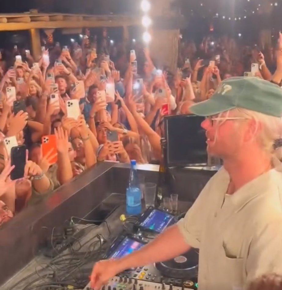 DJ at decks, crowd holding phones aloft